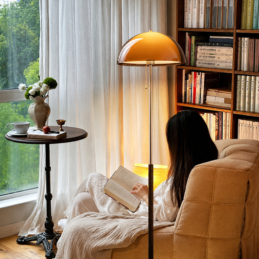 A modern floor lamp with a glossy dome shade in warm amber-orange and a polished silver metal pole