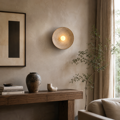 A round, shallow bowl-shaped wall sconce with a textured beige metal rim