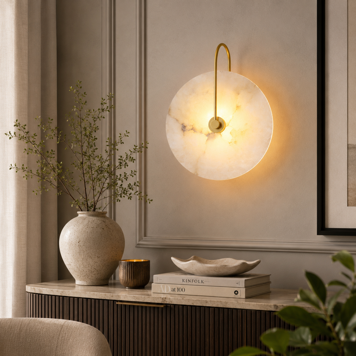 A modern circular wall sconce with a warm glowing white marble disc and a curved gold metal arm