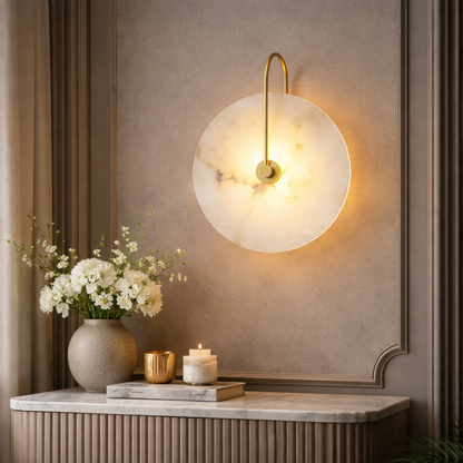 A modern wall sconce with a round white marble shade and a curved gold metal arm