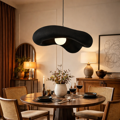 A modern abstract black pendant light hangs over a round wooden dining table
