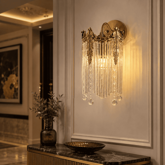 A wall-mounted sconce with a gold-toned metal frame and hanging clear crystal prisms