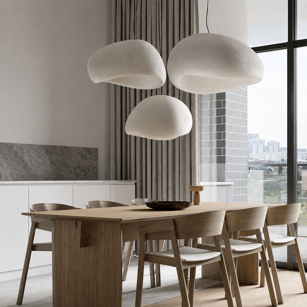Three organic-shaped white pendant lights hanging over a light wood dining table