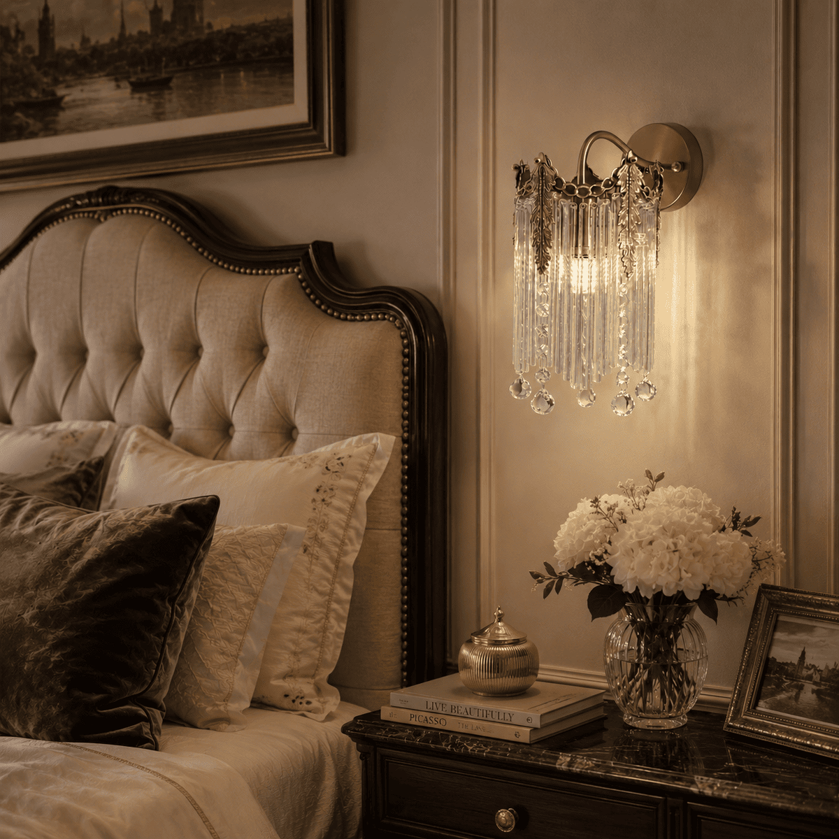 A warm, elegant wall-mounted crystal chandelier sconce with hanging teardrop pendants, illuminated in a cozy bedroom