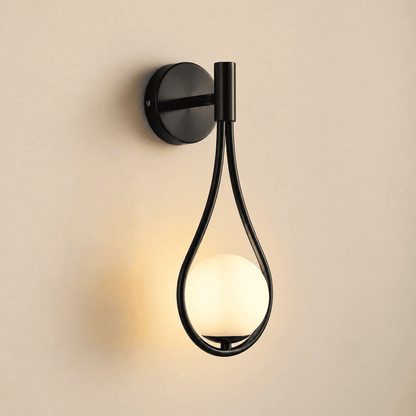 A modern black metal wall sconce with a teardrop-shaped frame and a glowing frosted glass globe