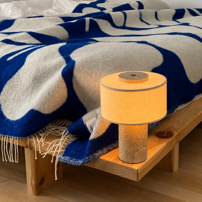 A modern table lamp with fabric shade and a textured stone base sits on a wooden nightstand