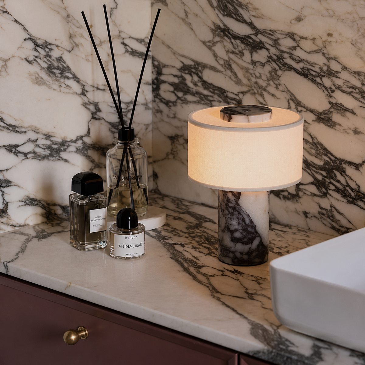A lit table lamp with a cream fabric drum shade and a dark marbled base