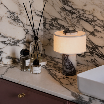A lit table lamp with a cream fabric drum shade and a dark marbled base