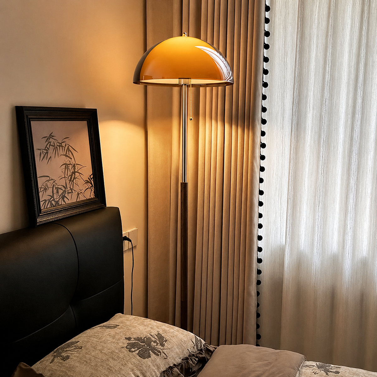 A modern floor lamp with a dome-shaped amber glass shade and a silver metal pole stands beside a bed