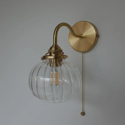 A wall-mounted light fixture with a ribbed clear glass globe shade, an arched brass-toned metal arm