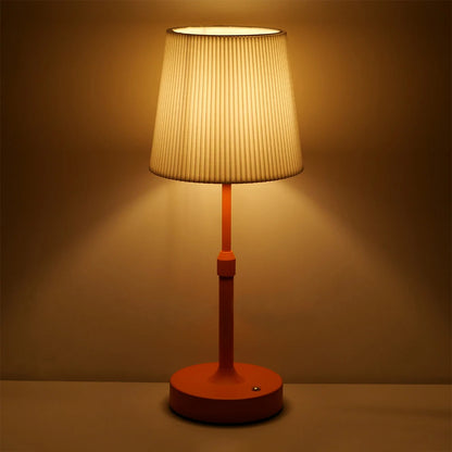 A table lamp with a pleated white fabric shade and a warm orange base