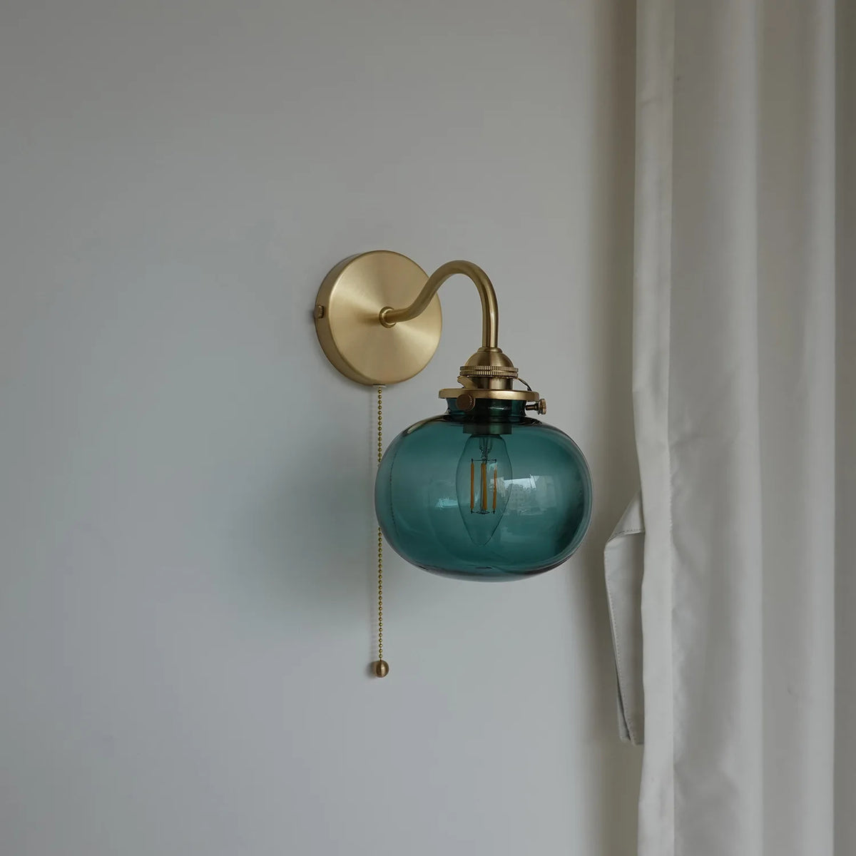 Wall-mounted lamp with blue glass shade and brass fixture on a plain wall