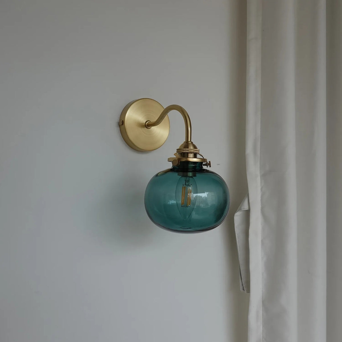Wall-mounted lamp with a teal glass shade and gold fixture on a plain wall
