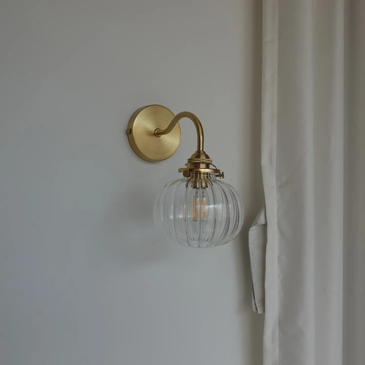 Gold wall sconce with a clear glass shade on a neutral wall