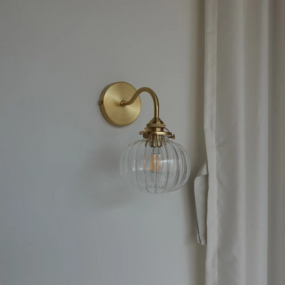 Gold wall sconce with a clear glass shade on a neutral wall