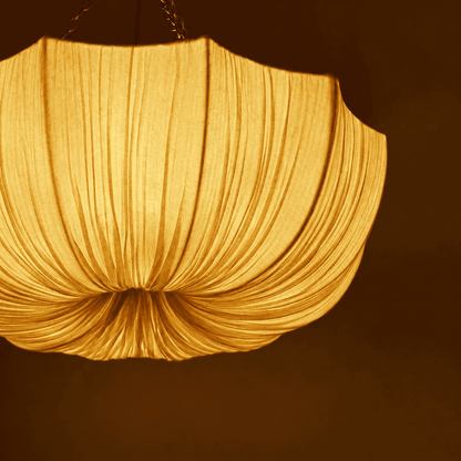 A close-up of a pleated fabric pendant light glowing with a warm golden-yellow light
