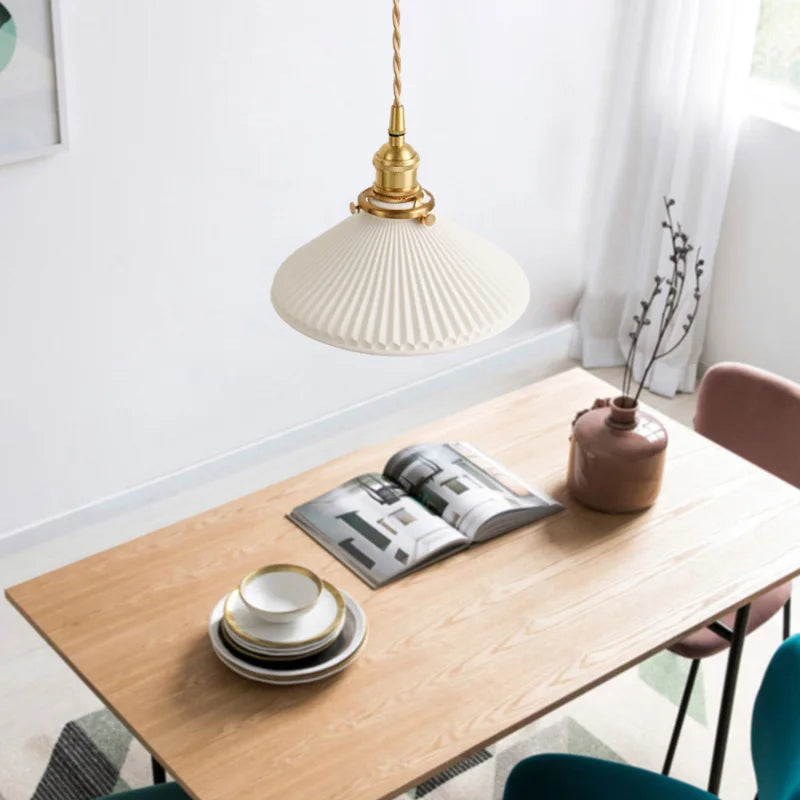 Wooden dining table with a lamp, books, and small vase in a bright room.