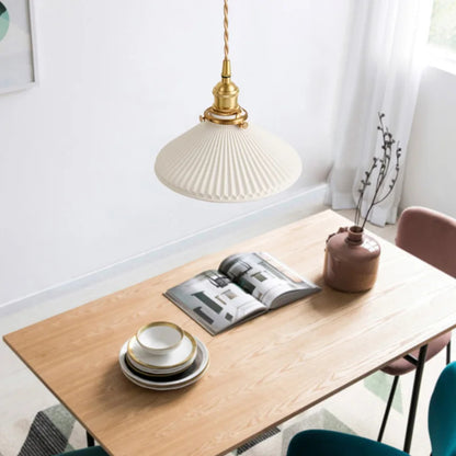 Wooden dining table with a lamp, books, and small vase in a bright room.