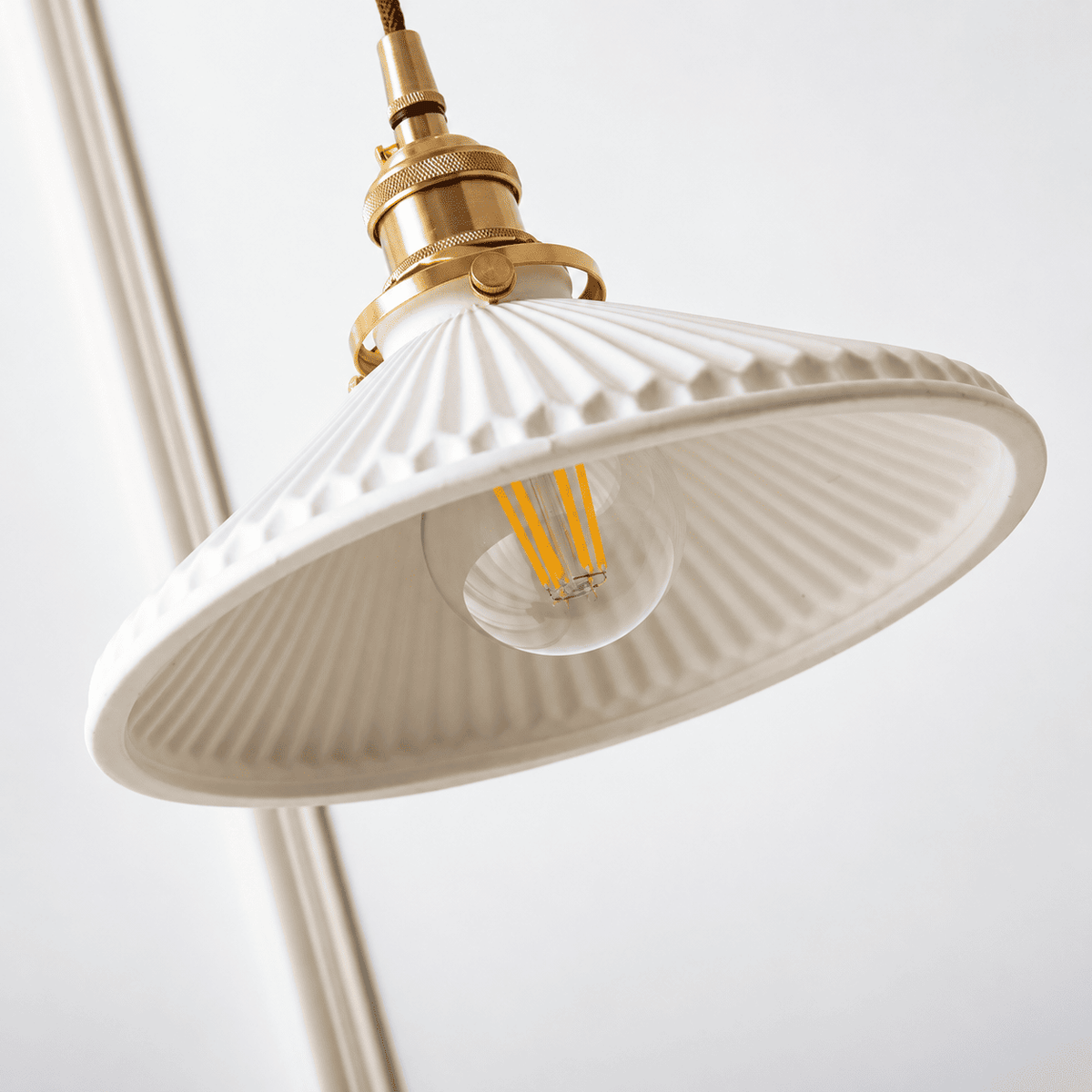 A close-up of a hanging pendant light with a white ribbed glass shade, a brass metal fixture